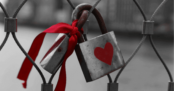 Padlock with a red heart on it locked to a fence.