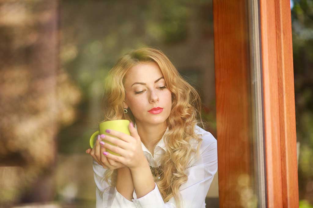 Thoughtful woman looking out a window holding a coffee cup.