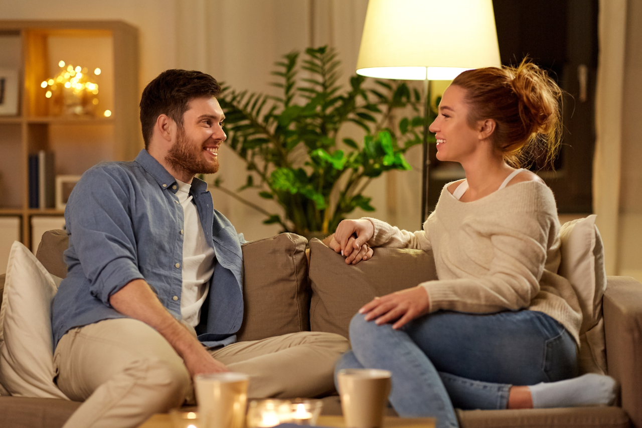 Man and woman sitting on sofa looking at each other smiling.