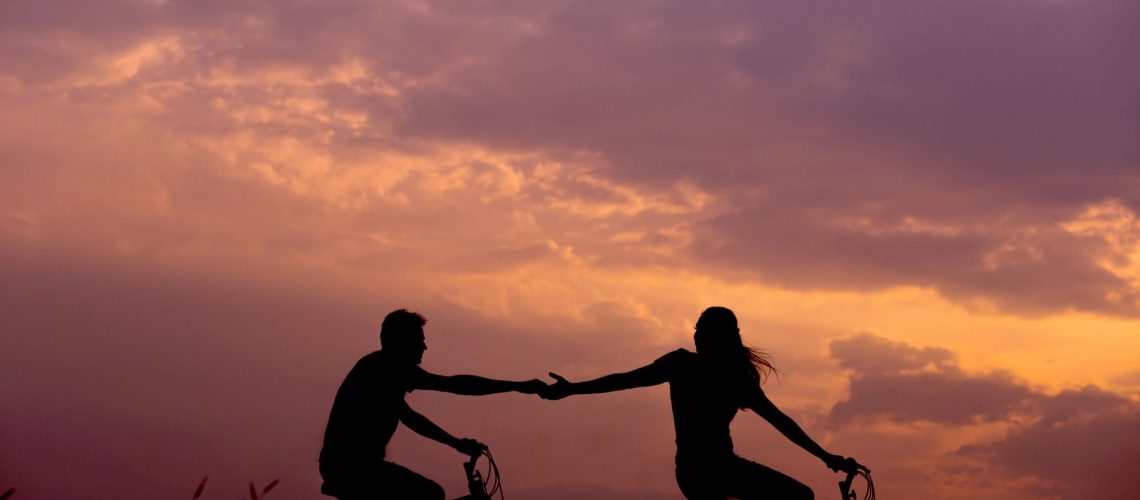 Couple riding bikes and holding hands in the sunset.